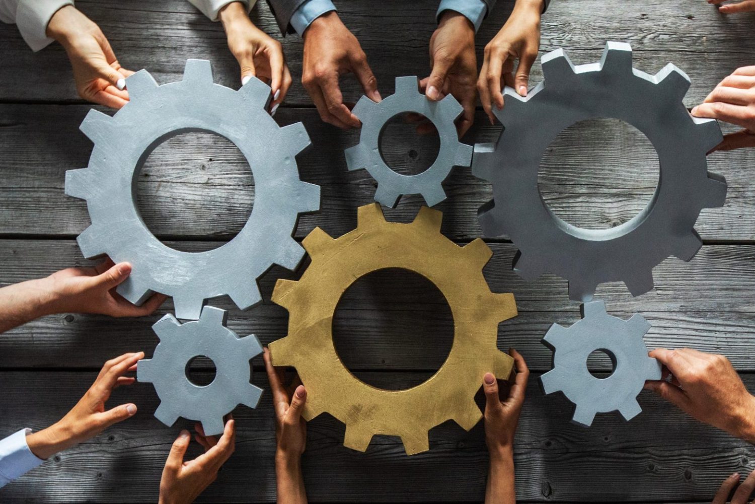 Group of business people joining together silver and golden colored gears on table at workplace top view